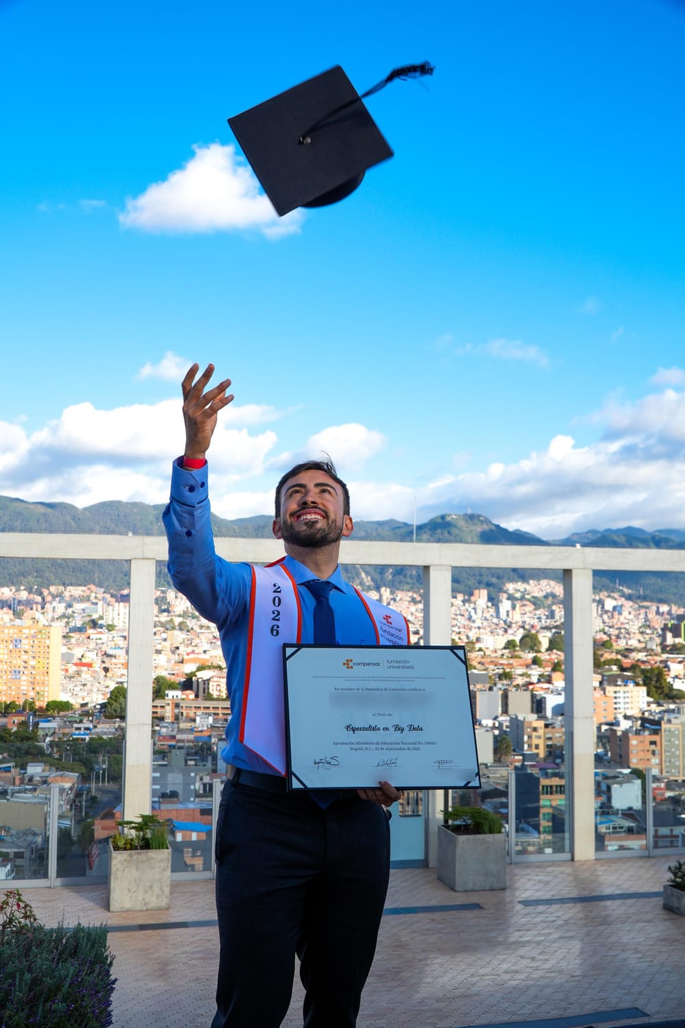 Gabo lanzando el birrete al cielo azul con el diploma en una mano, sobre una terraza con vista a Bogotá