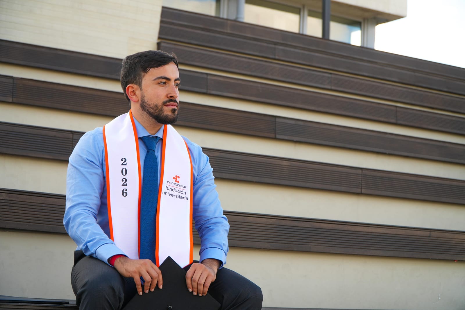 Gabo sentado en unas gradas de madera con la banda de graduación, mirando hacia un lado con expresión serena