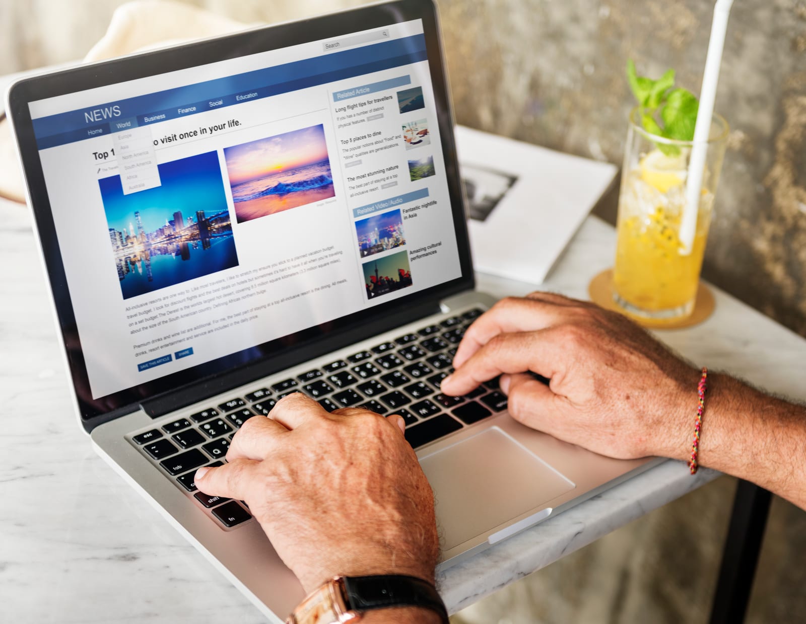 Manos escribiendo en un portátil que muestra una página web con noticias e imágenes